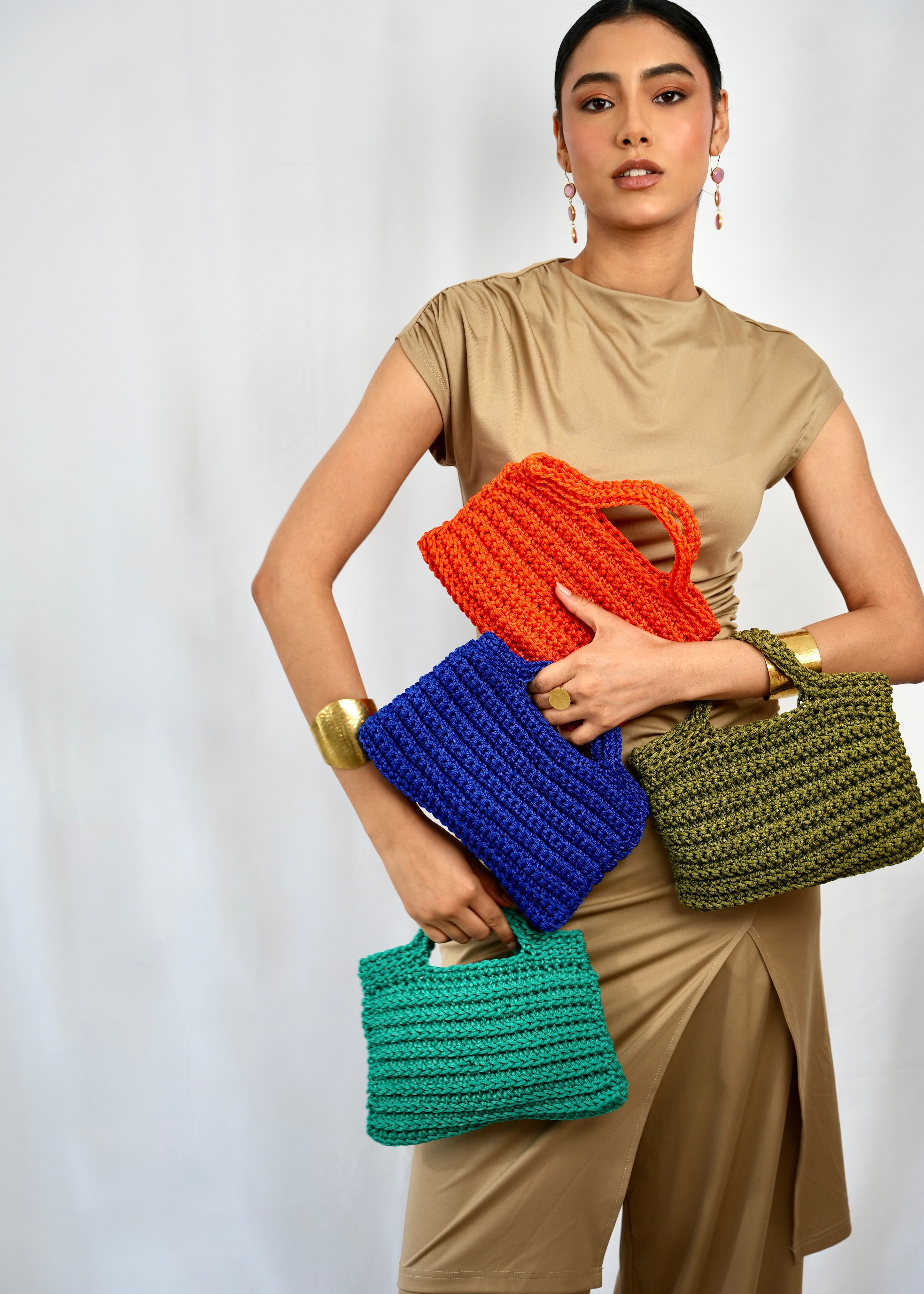 Several square blue crochet bags hand-carried by a studio model