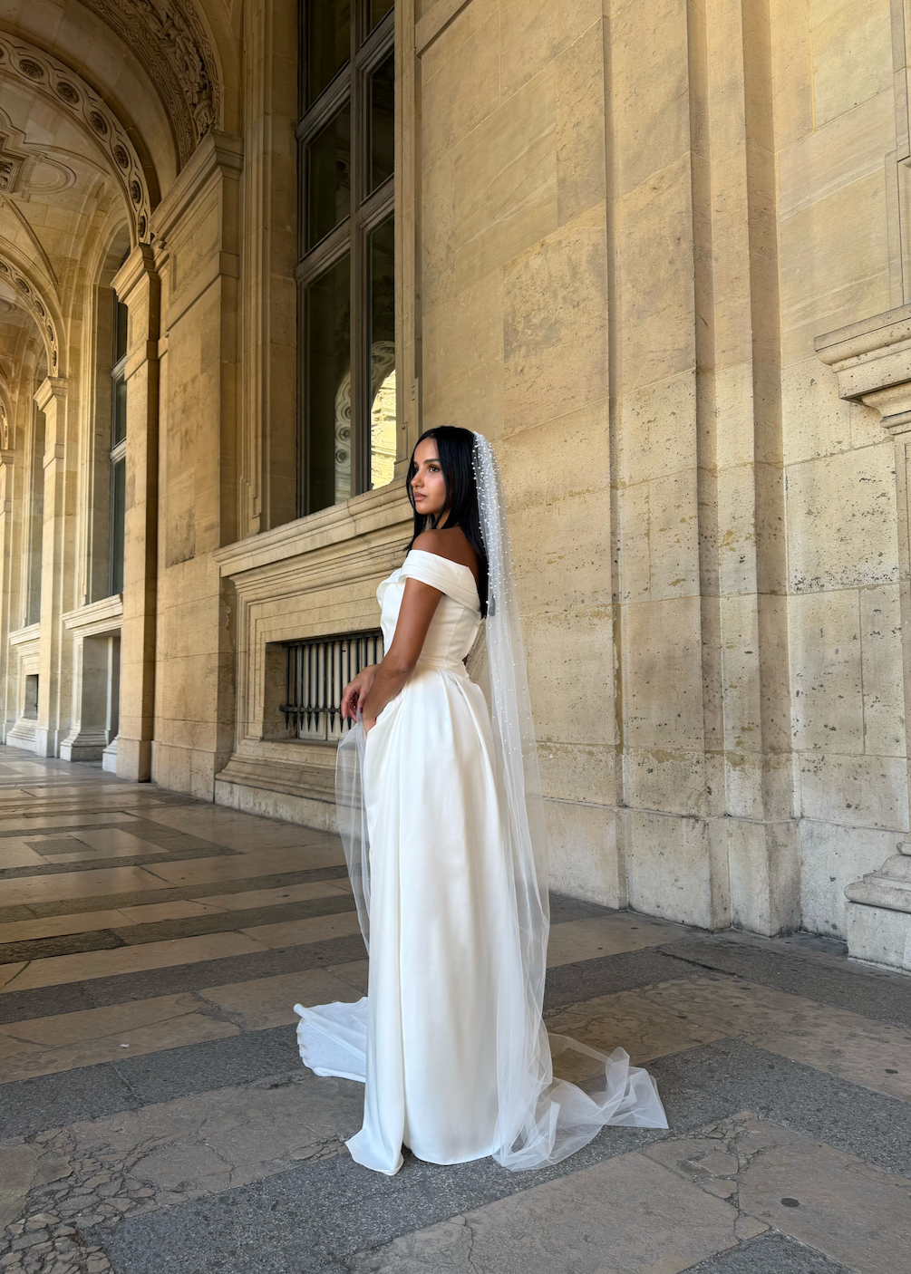Profile of a bride wearing a flowing tulle veil with embroidered beads adding texture.
